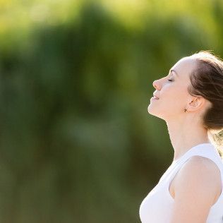 Woman with eyes closed, tilted head, enjoying sunlight. Green background, white top.