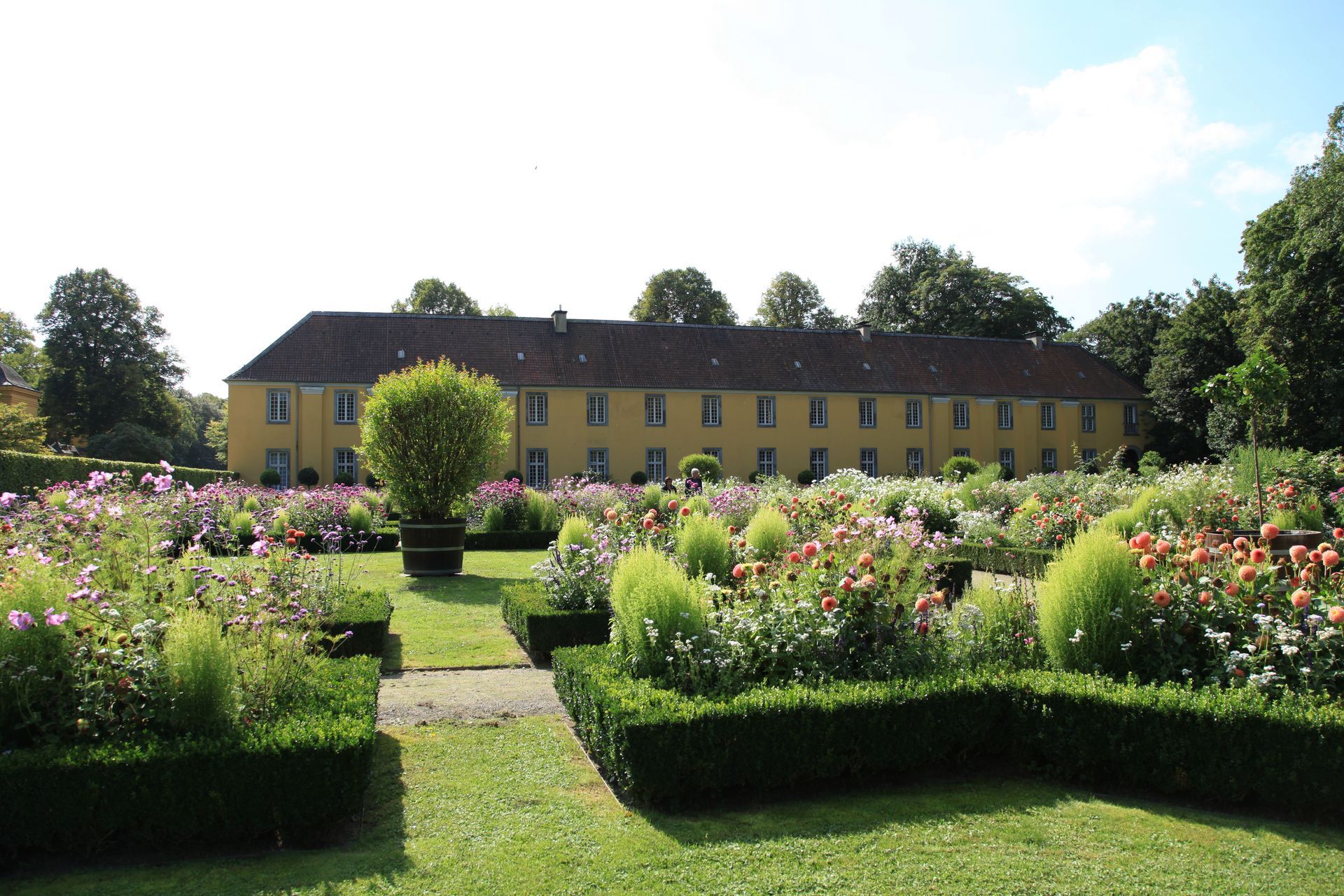 Formal garden with colorful flower beds and a long yellow building in the background
