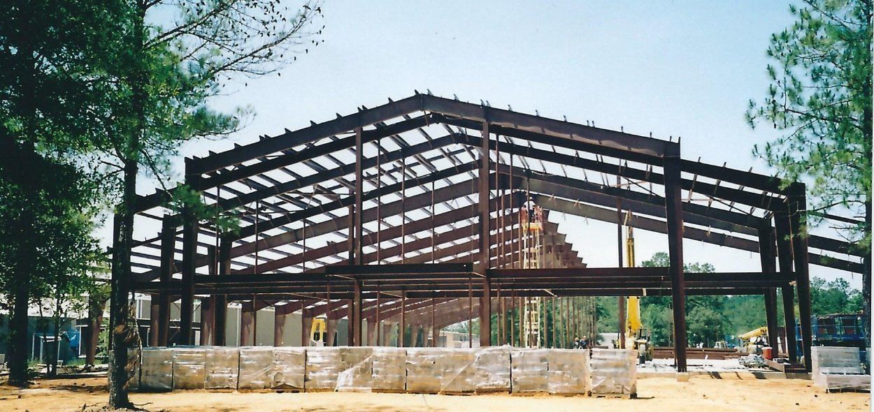 Open steel building frame under construction on a sunny site with trees around it