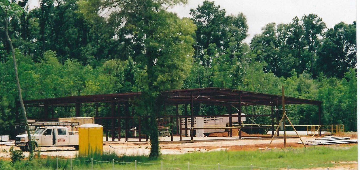 Open-sided pavilion with picnic tables in a wooded park, with a white truck and yellow portable toilets nearby