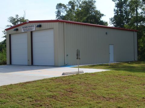 White metal storage building with red roof trim and two garage doors beside a concrete driveway.