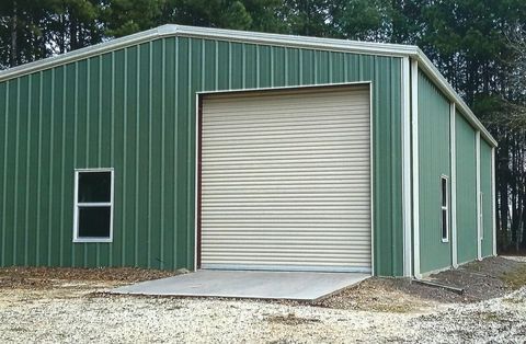 Green metal garage with a large roll-up door and a small side window
