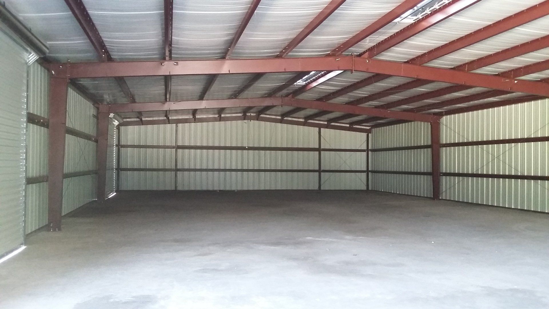 Empty metal warehouse interior with red steel beams and a concrete floor