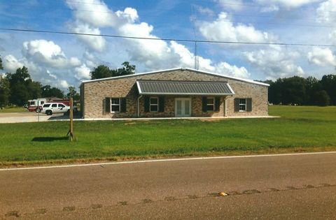 Single-story brick building on a grassy lot under a cloudy sky, with a road in the foreground.