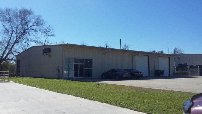 Single-story beige building with glass doors, parked cars, and a grassy lot under a clear blue sky.