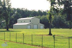 White barn in a green field behind a wire fence, with trees in the background.