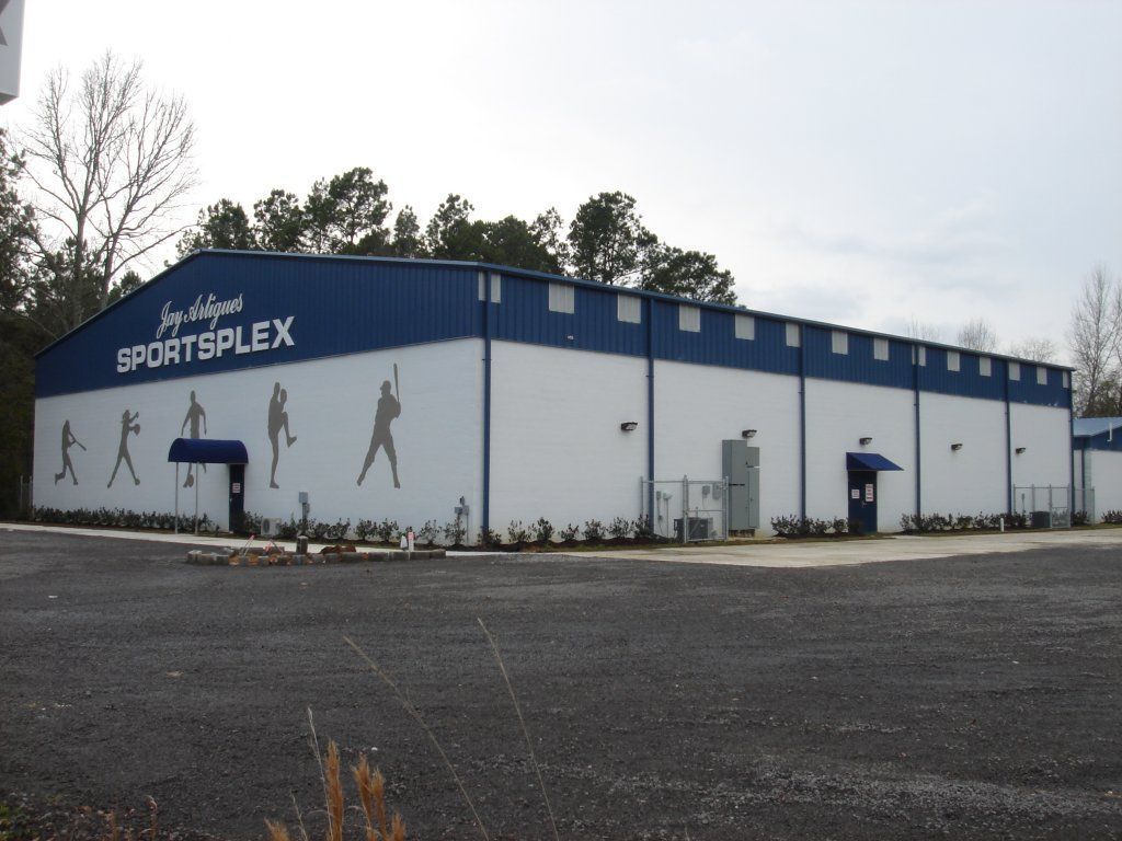 Exterior of a blue-and-white sportsplex building with athletic wall murals and a parking lot in front