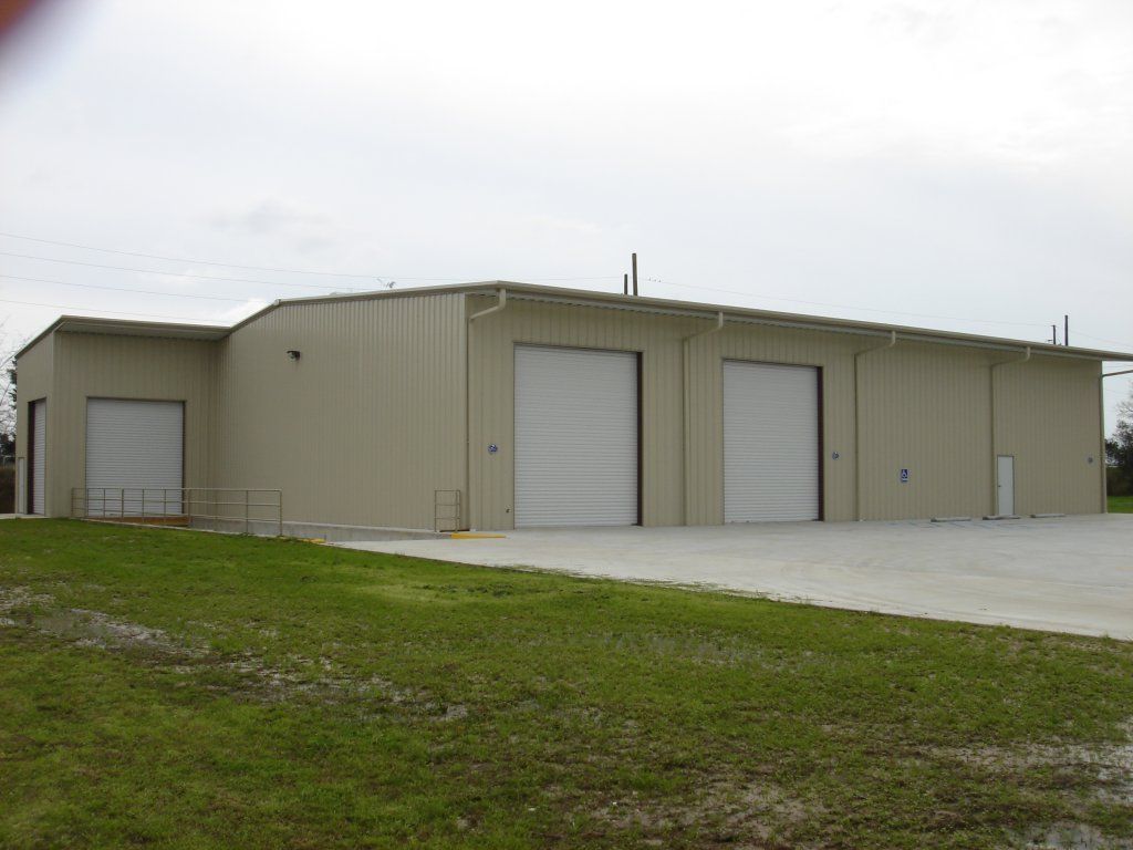 Tan industrial building with two white garage doors on a grassy lot under an overcast sky