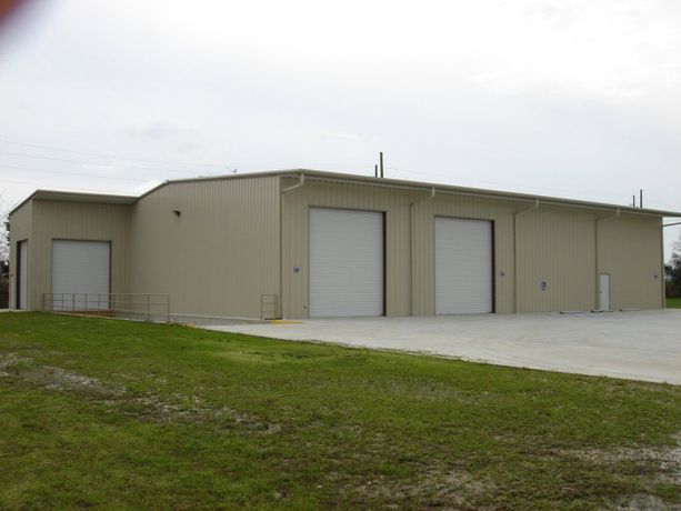 Tan industrial building with two white garage doors on a grassy lot under an overcast sky