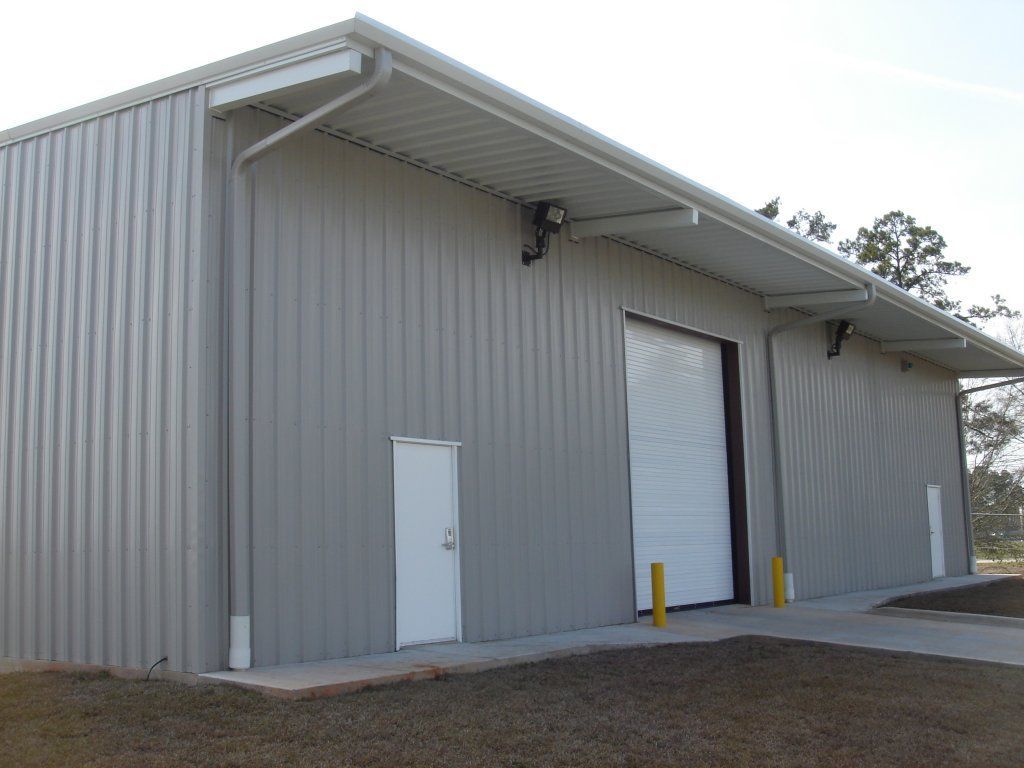 Gray industrial warehouse exterior with white roll-up door and small side door under a metal awning