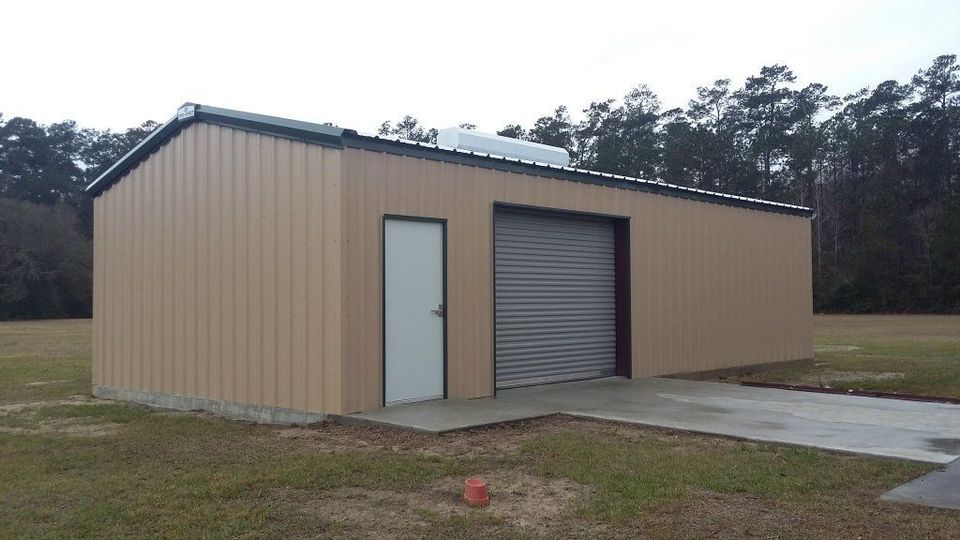 Tan metal storage building with white door and roll-up garage door beside a concrete driveway.