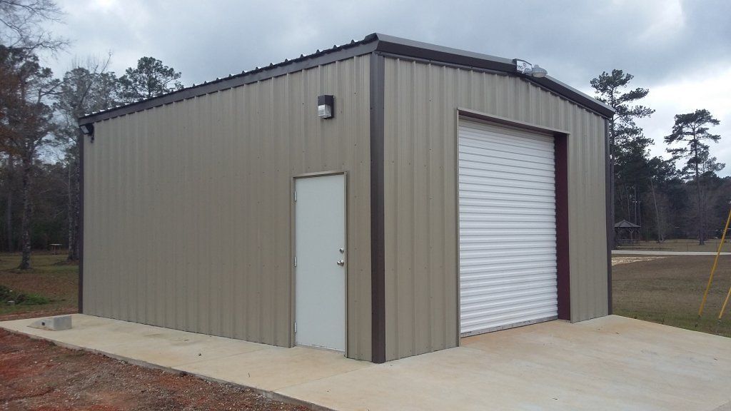Tan metal utility building with white roll-up garage door and side entry door on concrete slab.