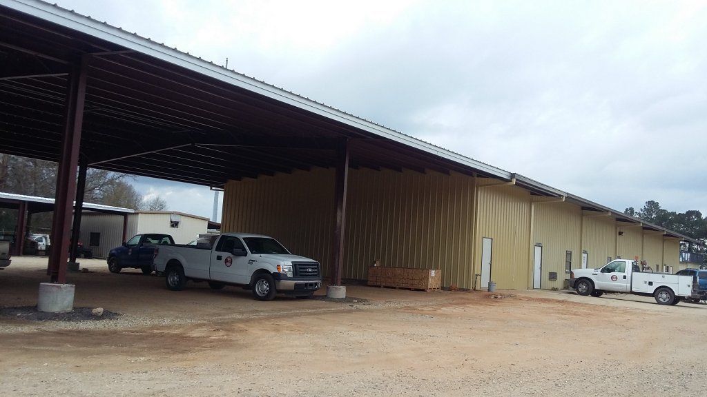 Rural metal shed with parked pickup trucks on a gravel lot under an overcast sky