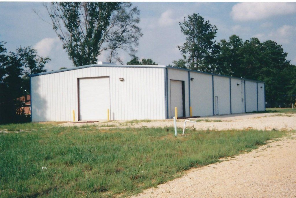 White metal storage building on a dirt lot with grass and trees around it.