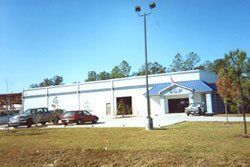 Single-story white building with blue awnings and parked cars on a sunny day
