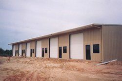 New metal warehouse building with roll-up doors on a dirt lot