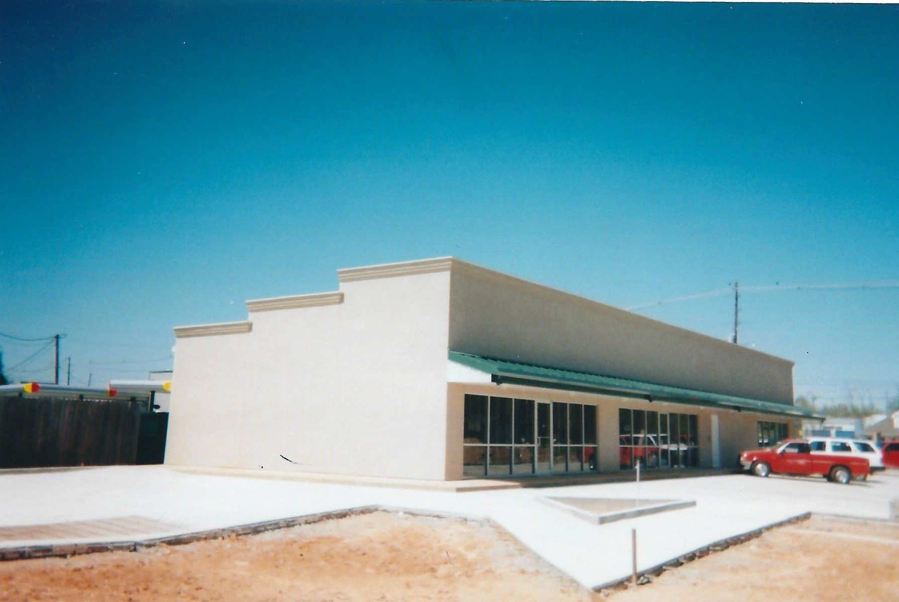 Low beige commercial building with glass front and a red car parked outside under a clear blue sky