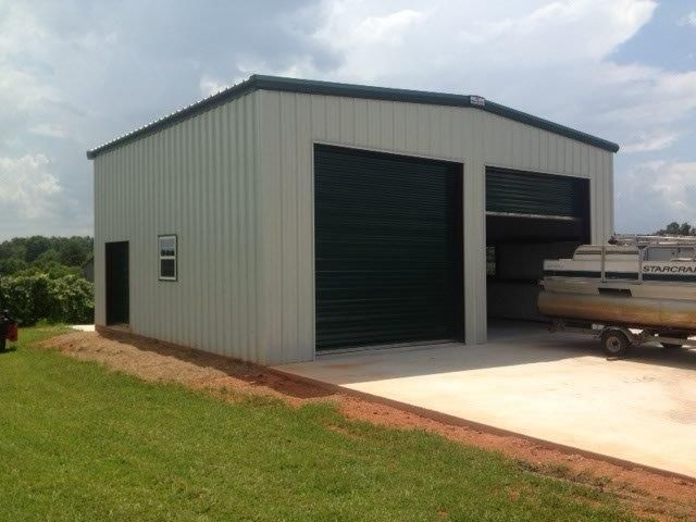 Gray metal storage shed with two open garage doors and a concrete driveway beside a grassy lawn