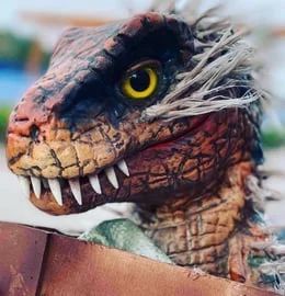 Close-up of a toy dinosaur with orange scales, yellow eye, and sharp teeth