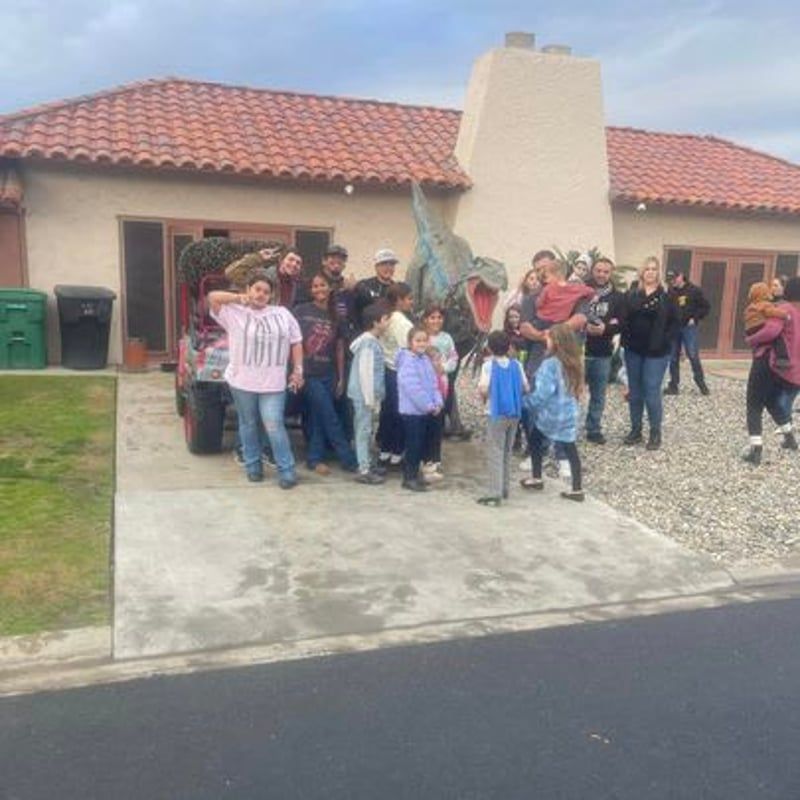 Group of people posing outside a stucco house with a red tile roof, on a driveway and lawn.