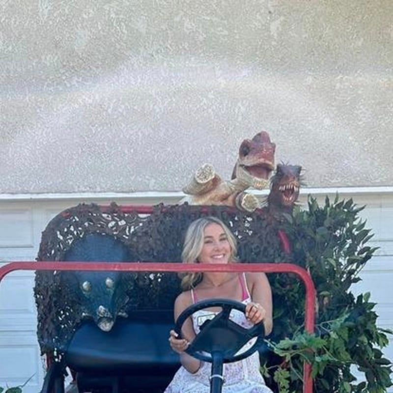 Woman smiling in a golf cart decorated with holiday greenery and a dinosaur figure behind her