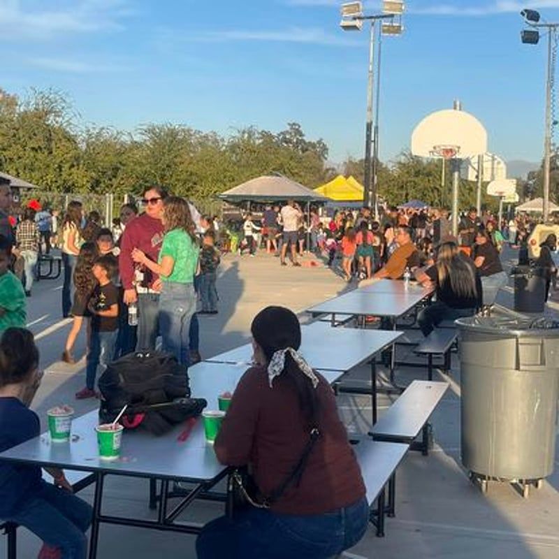 Crowded outdoor event with people at picnic tables under a clear sky, with a yellow tent and white dome in the background