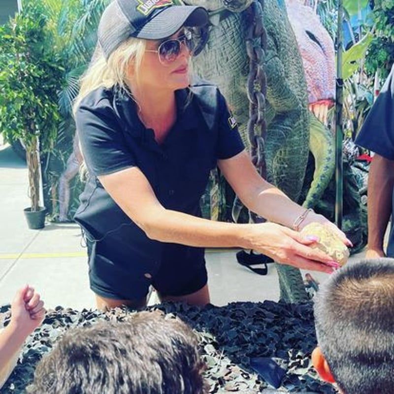 Woman in black shirt feeding a large reptile at an outdoor wildlife exhibit