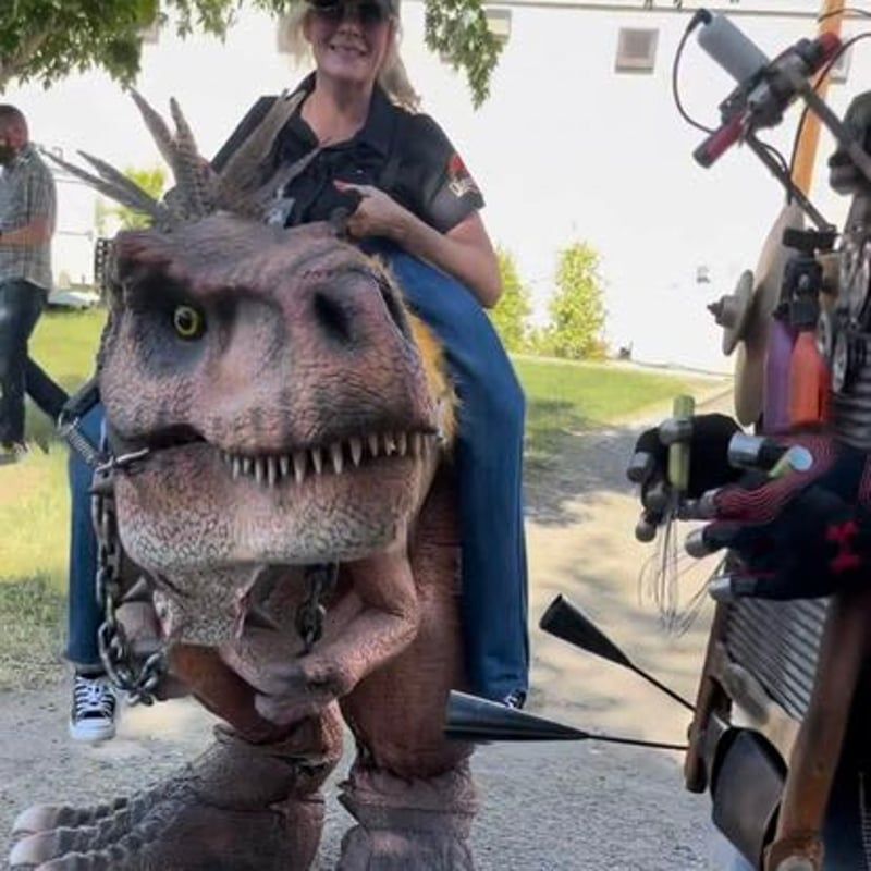 Person riding a realistic dinosaur costume at an outdoor event