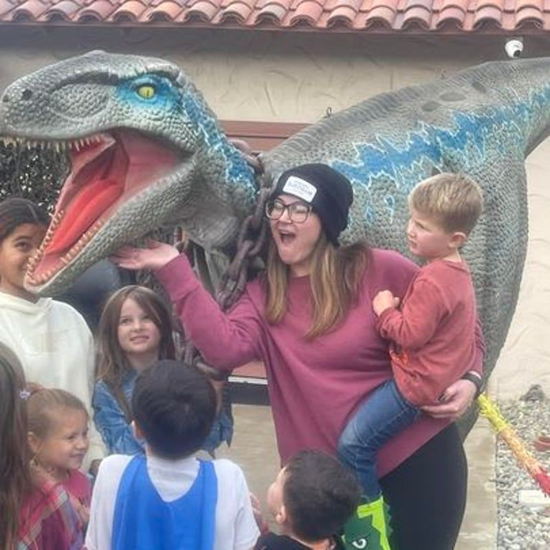 Woman posing with children beside a large blue dinosaur statue, all smiling outdoors.