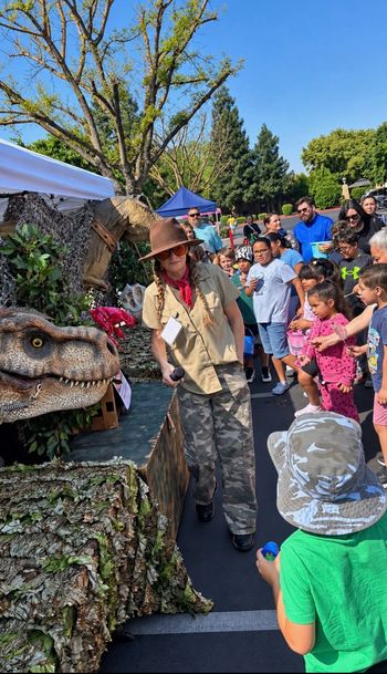 Large dinosaur statue facing a crowd of children outdoors at a school event