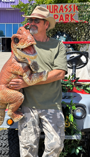 Man holding an orange dinosaur statue in front of a Jurassic Park sign outdoors