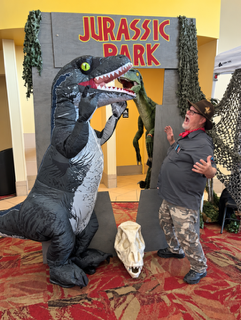 Person in dinosaur costume poses by a “Jurassic Dark” doorway with a small skull prop.