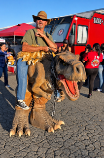 Man in cowboy hat riding a realistic dinosaur costume at an outdoor event