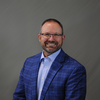 Smiling man in a blue checkered blazer and light blue shirt against a gray backdrop