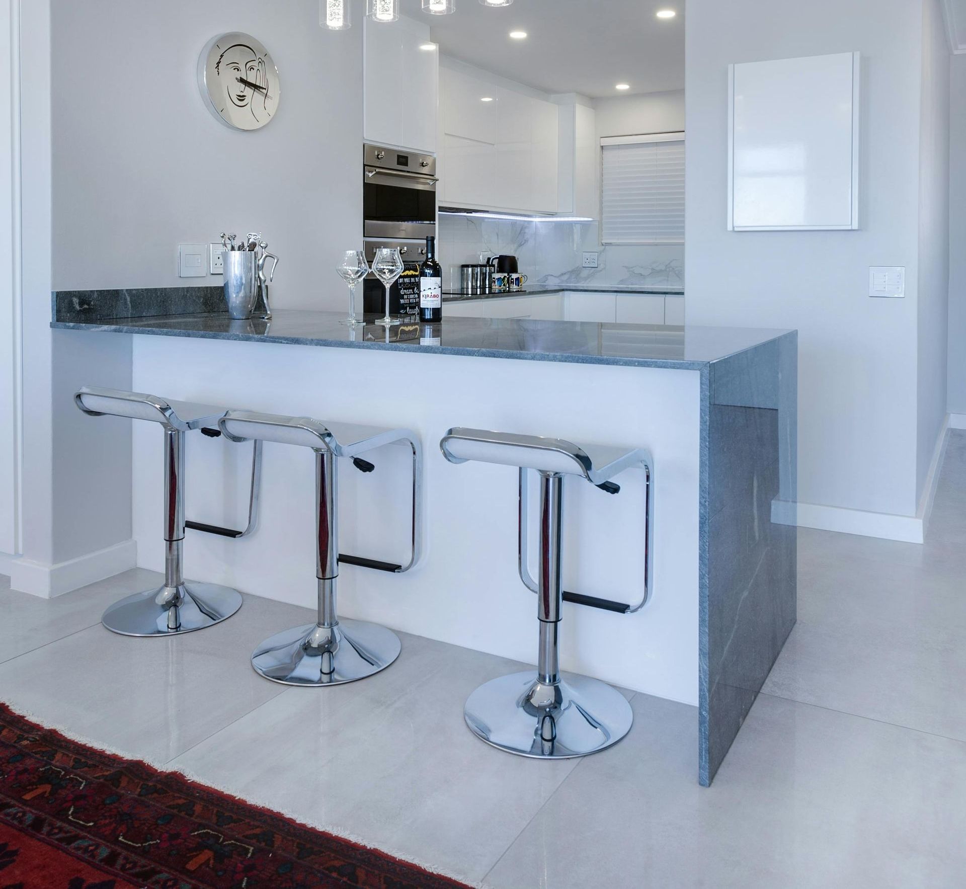 Kitchen with three bar stools and a wall clock