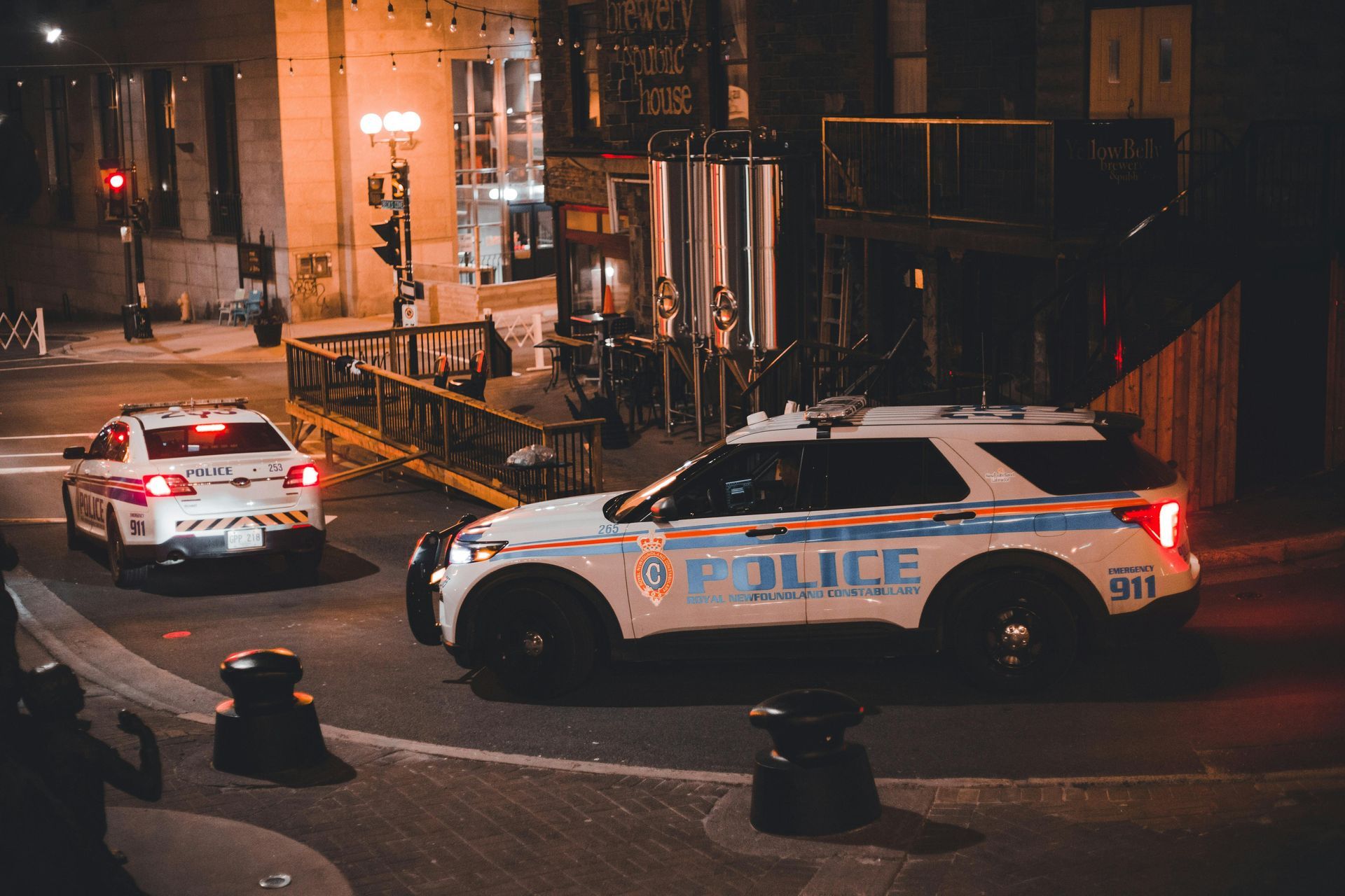 Two police SUVs parked on a city street at night, lights off, with brick buildings in the background