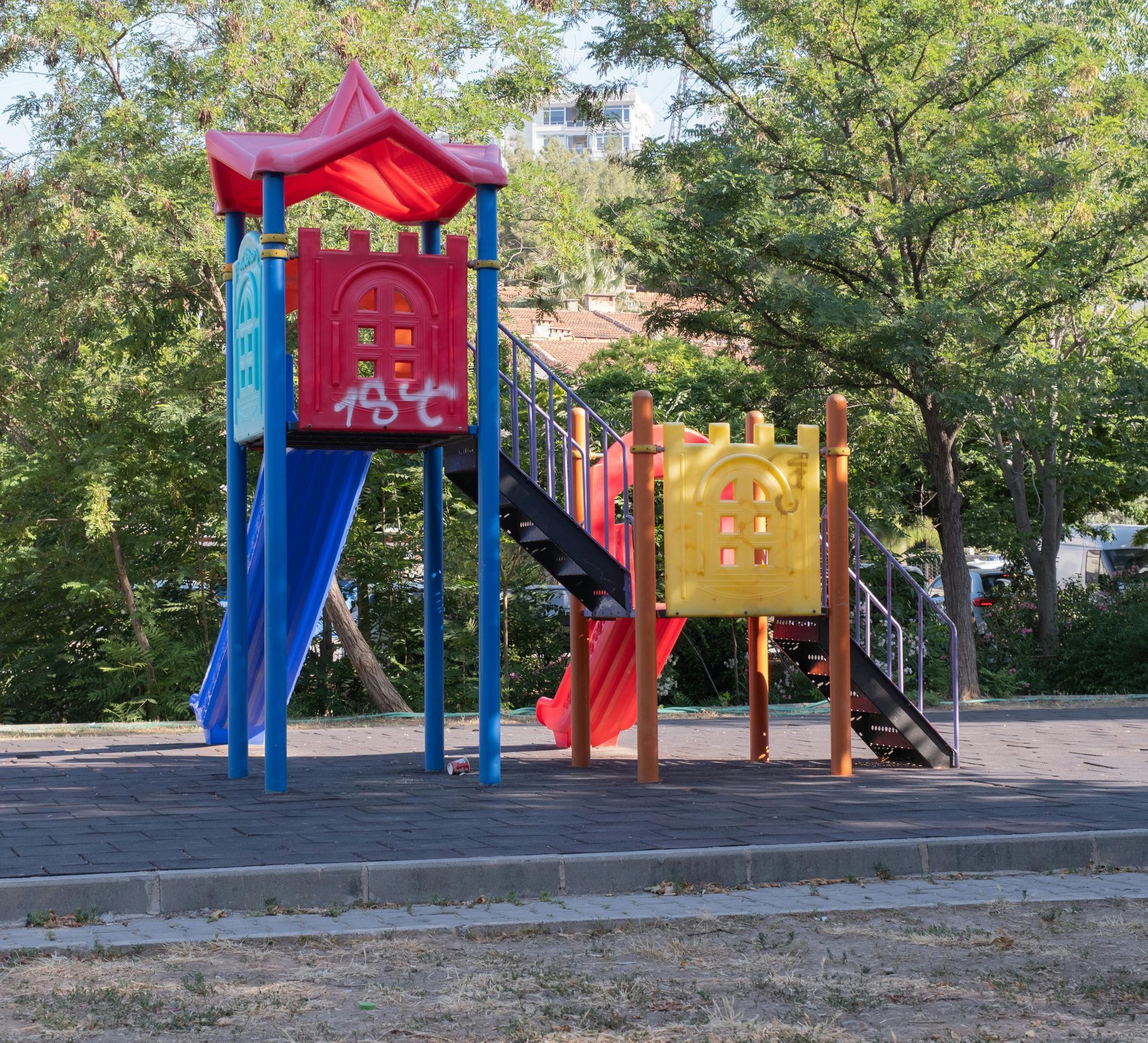 Playground structure with slides and steps, set in a park with trees.