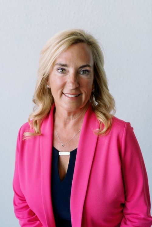 A woman is wearing a pink jacket and smiling for the camera.
