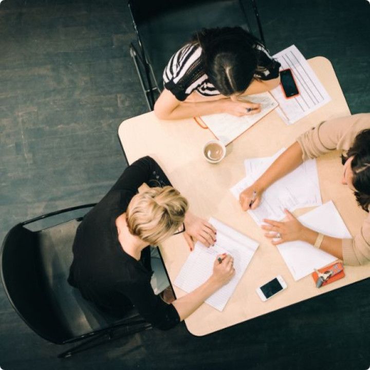 Three people are sitting at a table with papers and a cell phone