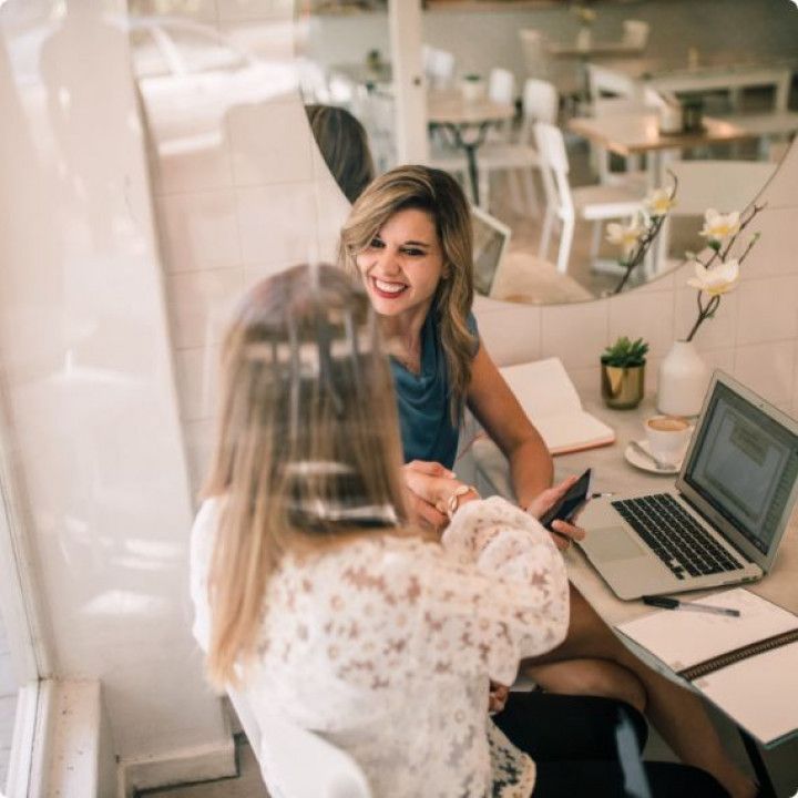 Two women are shaking hands while sitting at a desk with a laptop.