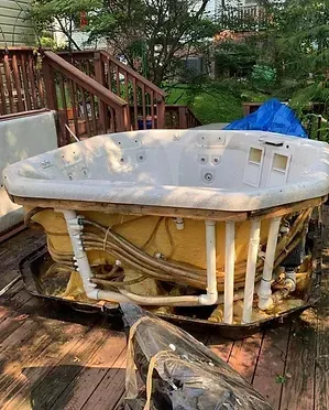 A disassembled hot tub on a wooden deck. Visible components include pipes, wiring, and insulation.