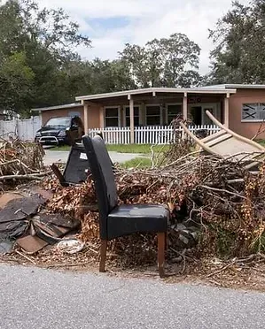 Pile of debris with a chair in front of a house, possibly after a storm.