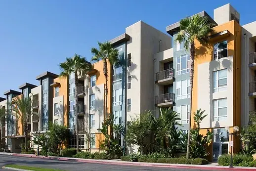 Multi-story apartment building with palm trees and a blue sky.