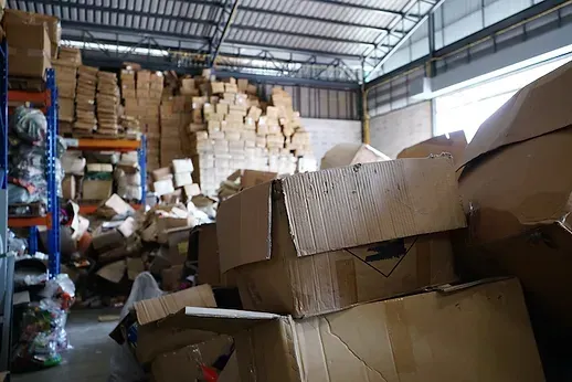 Warehouse interior with cardboard boxes and stacked shelves, appearing disorganized and cluttered.