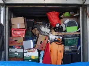 Storage unit packed with assorted boxes, crates, appliances, and clothing.