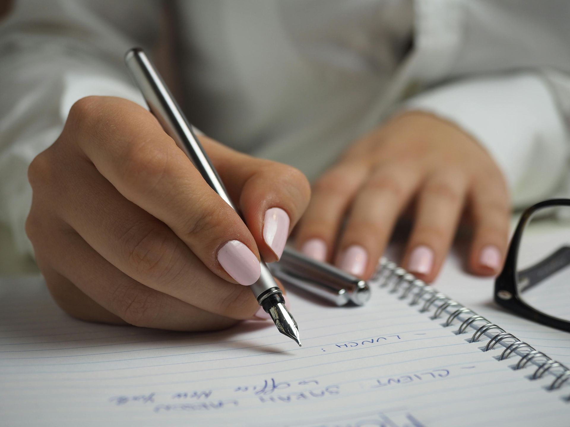 Person writing with a fountain pen in a notebook. Close-up on hands with pink nails.