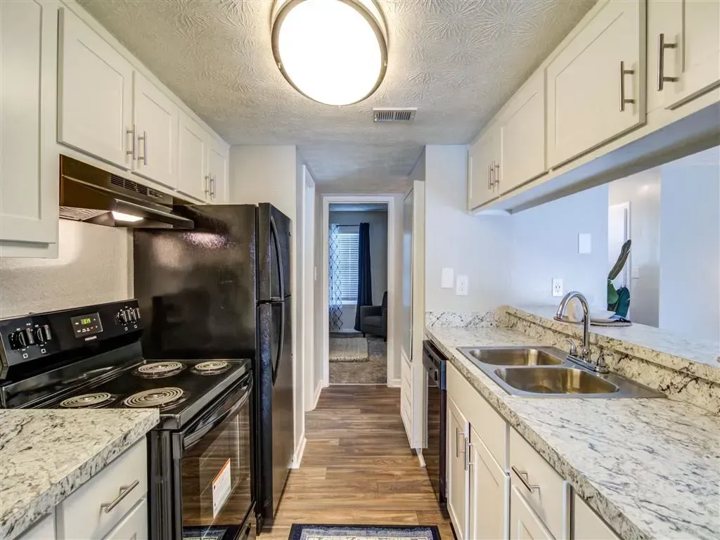 Narrow white kitchen with black appliances, granite counters, and wood-look flooring.