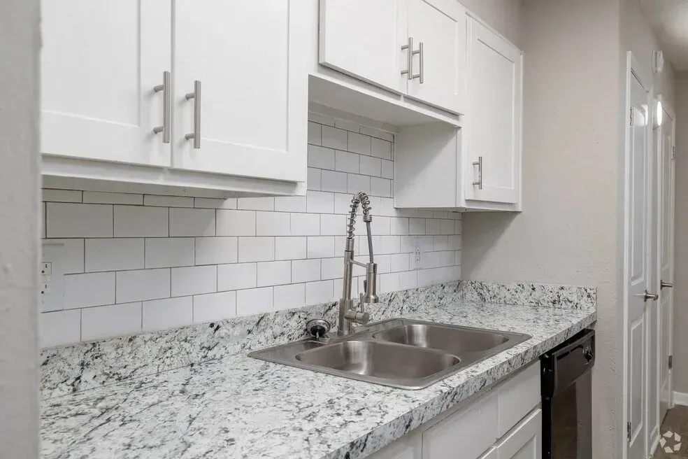 Modern white kitchen with speckled granite countertop, stainless sink, and white cabinets