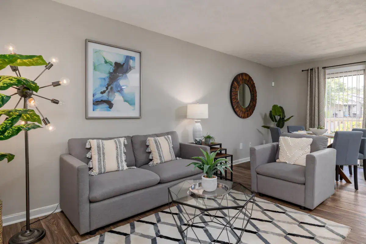 Modern living room with gray sofa, armchair, patterned rug, and large window.