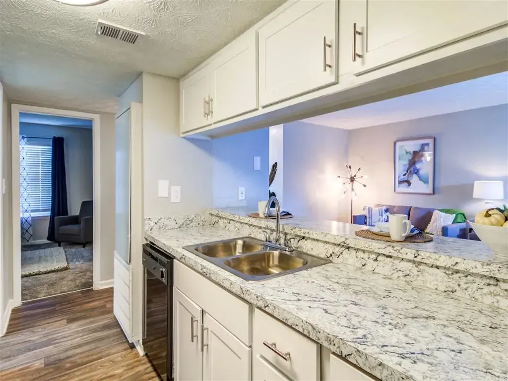 Bright kitchen with granite counters, white cabinets, and a hallway view into a living room.